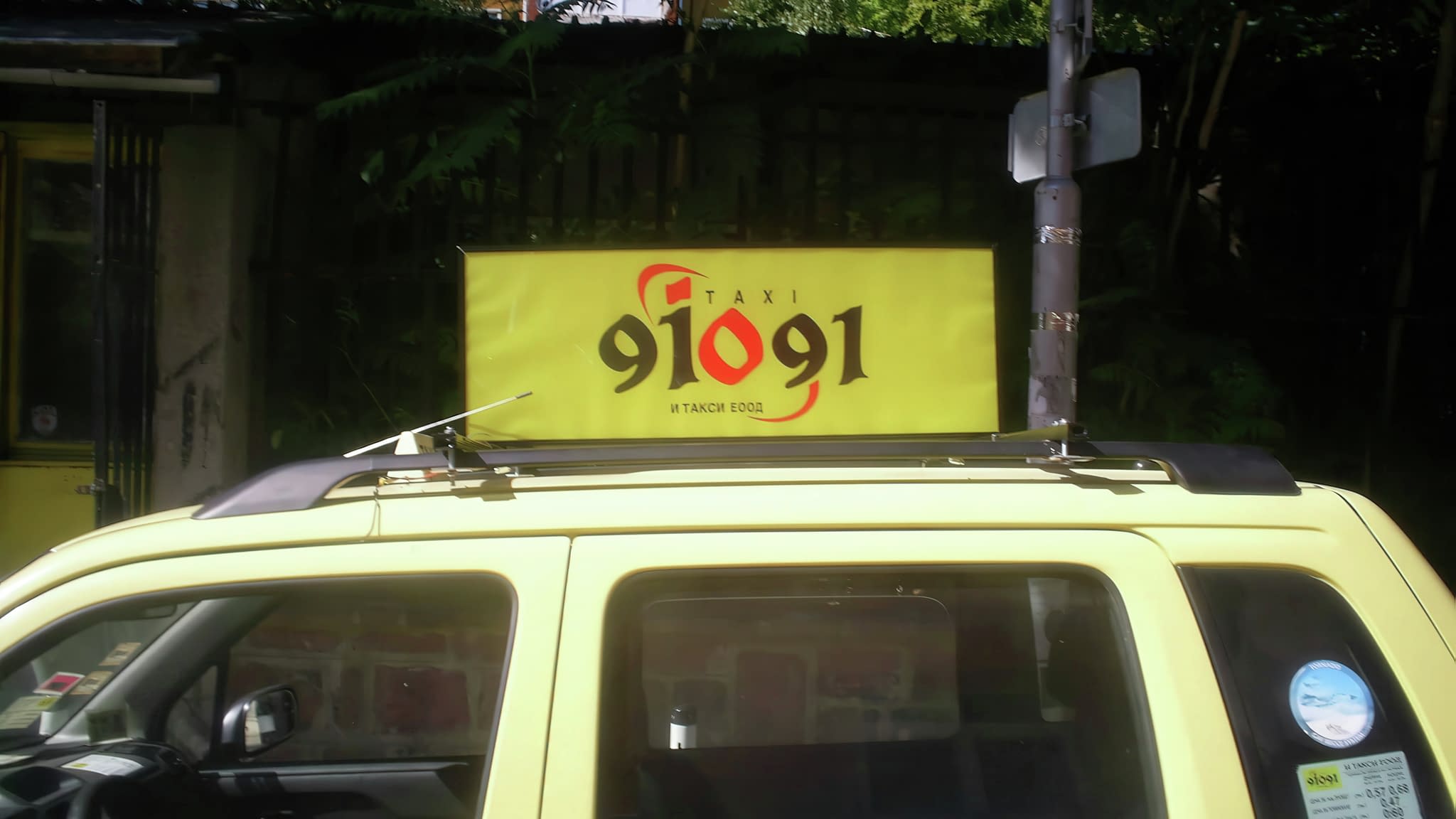 Реклама върху автомобил – жълто такси със светеща жълта табела на покрива с номер „91091“ и логото на И Такси ЕООД.