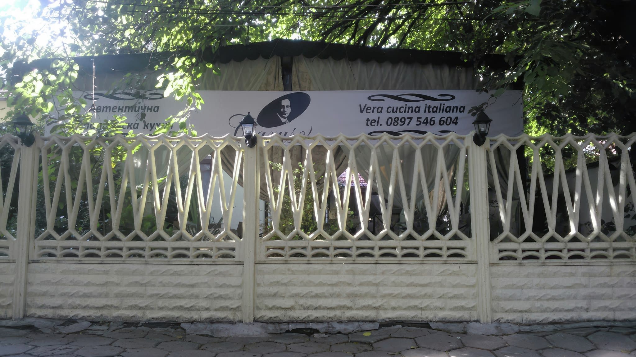 Рекламен транспарант от винил за италиански ресторант, окачен на ограда с надпис „Vera cucina italiana“ и телефон за резервации.