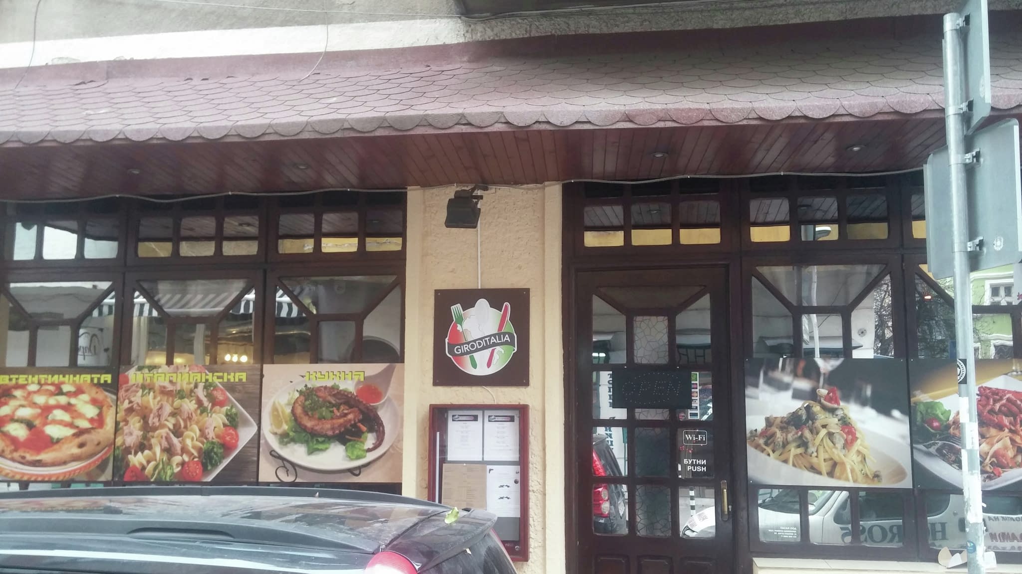 Фасада на италиански ресторант с двуезична табела и витрини със снимки на пица, паста и морски дарове – пример за ефективно брандиране на витрини.