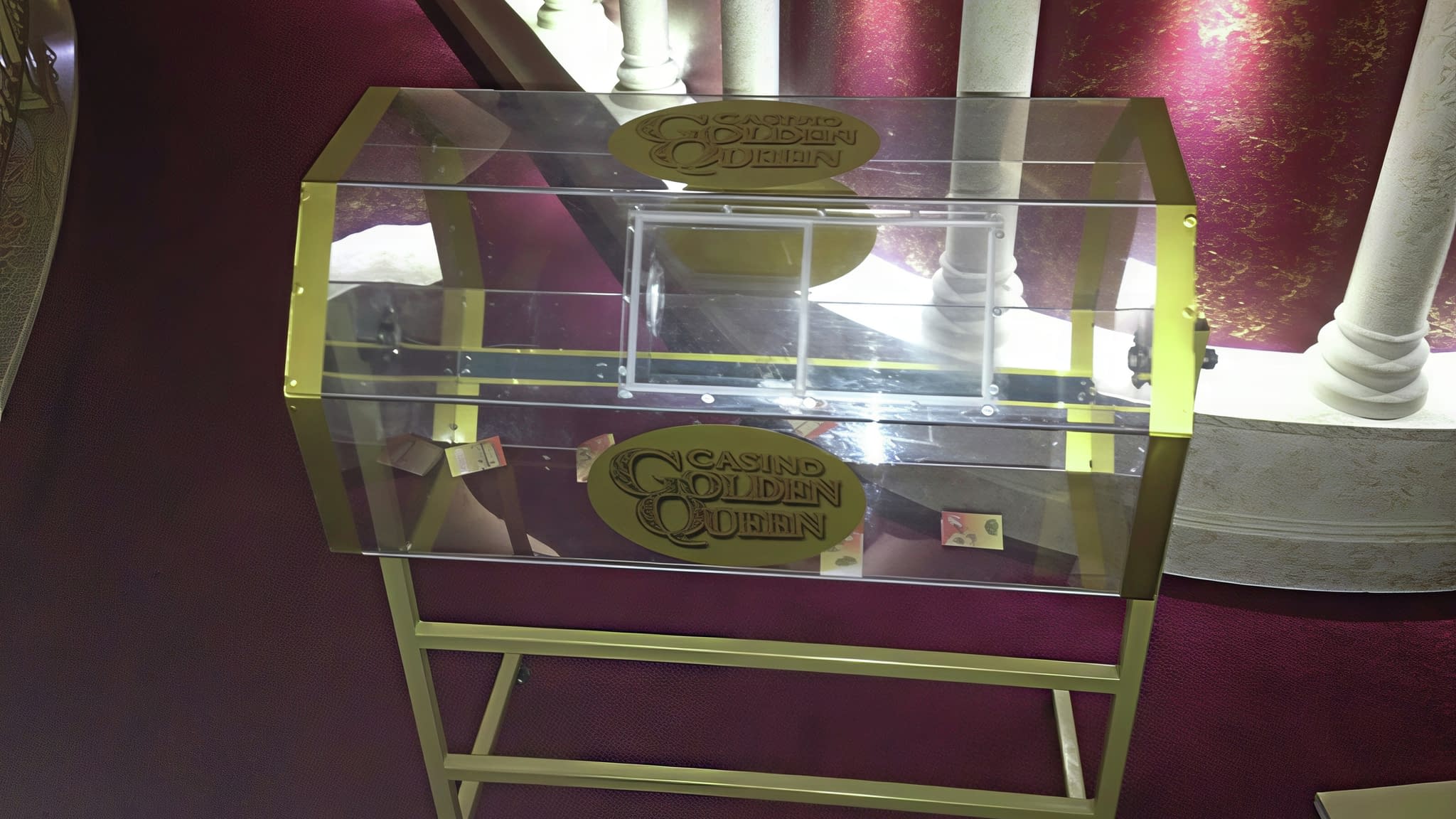 Прозрачна акрилна сфера за томбола с метална рамка и златисти декоративни елементи, поставена върху червен килим в елегантна обстановка – пример за изработка на томболна сфера за събития.