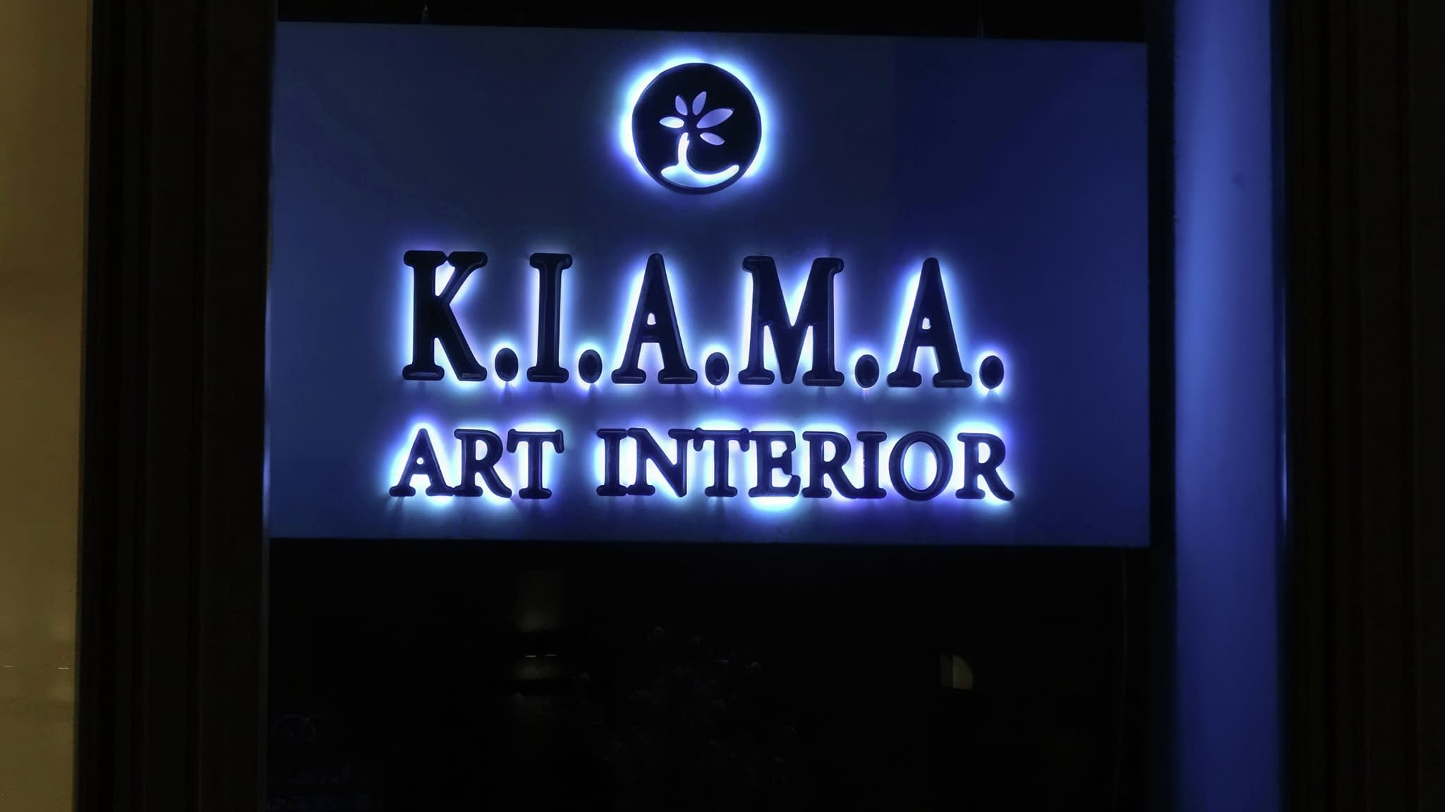 Светеща интериорна табела с надпис ‘K.I.A.M.A. Art Interior’ в синьо осветление със стилизирано лого – модерен дизайн за вътрешни рекламни решения.