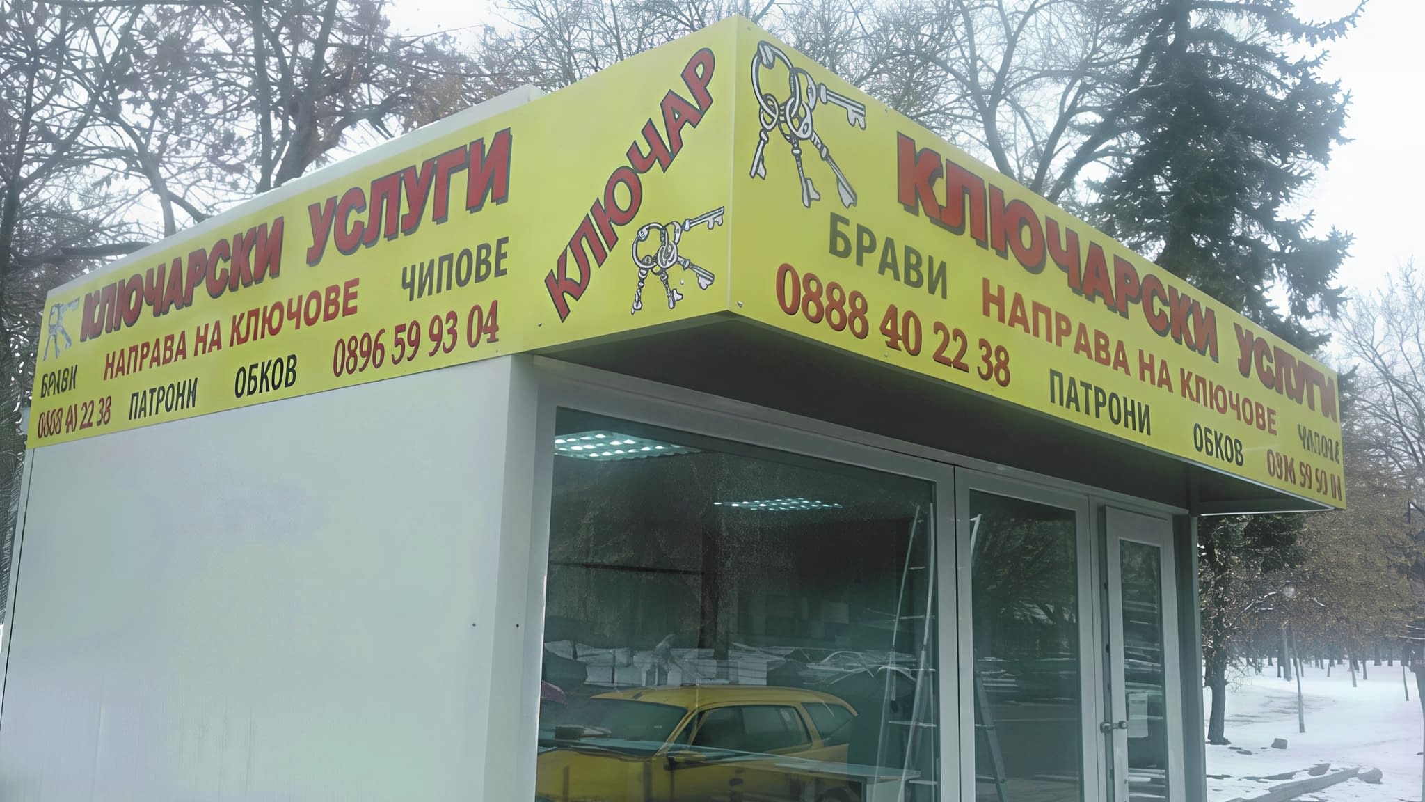 Жълта информационна табела за ключарски услуги с контактна информация и предлагани услуги като направа на ключове, чипове и брави.
