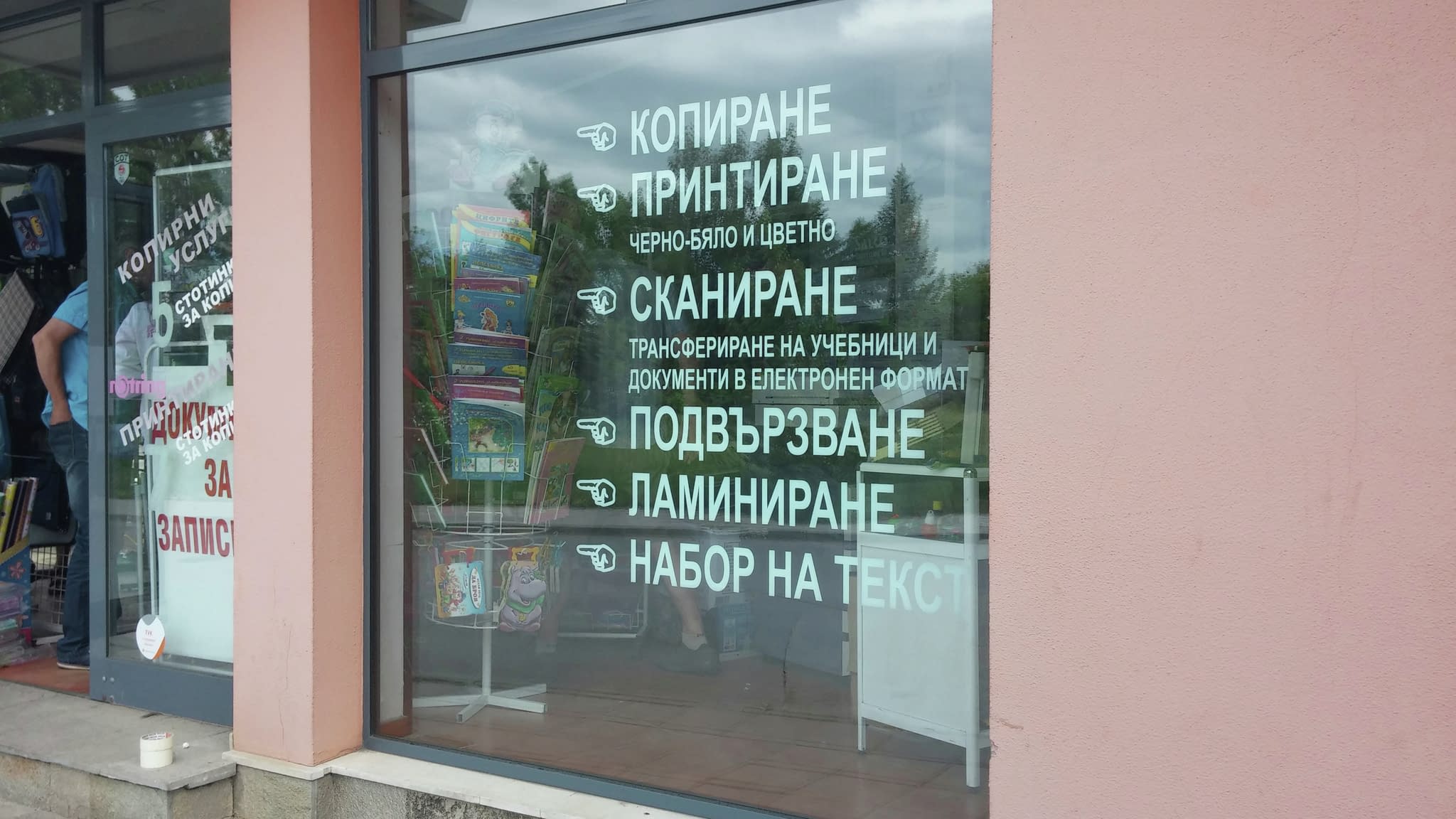 Витрина с рекламен надпис от фолио, изброяващ предлагани услуги - копиране, печат, сканиране, подвързване, ламиниране и набор на текст.