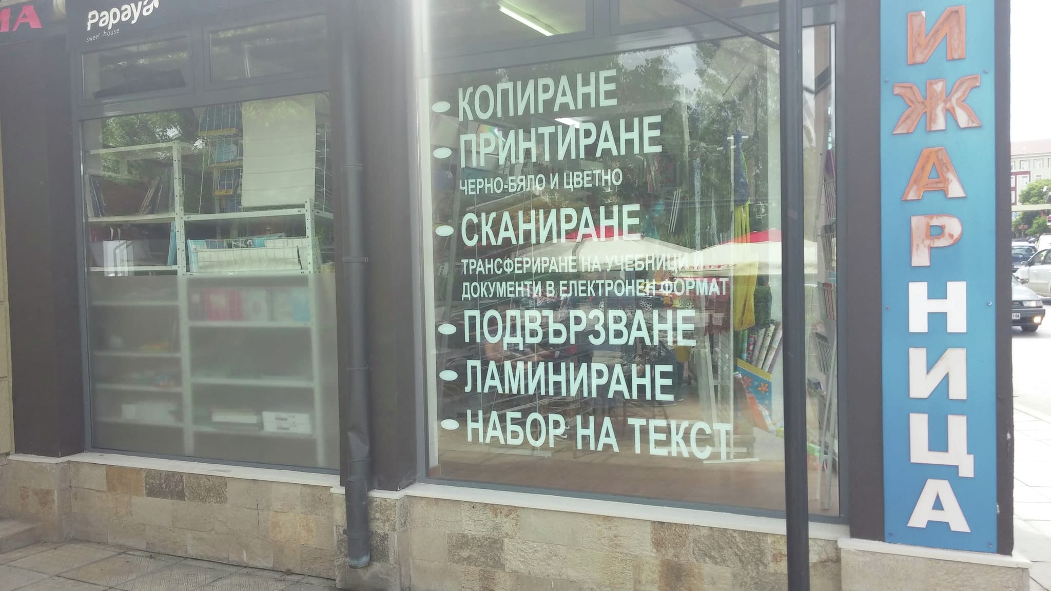 Витрина на печатница с рекламен надпис от фолио, изброяващ основни услуги - копиране, печат, сканиране, подвързване, ламиниране и набор на текст.