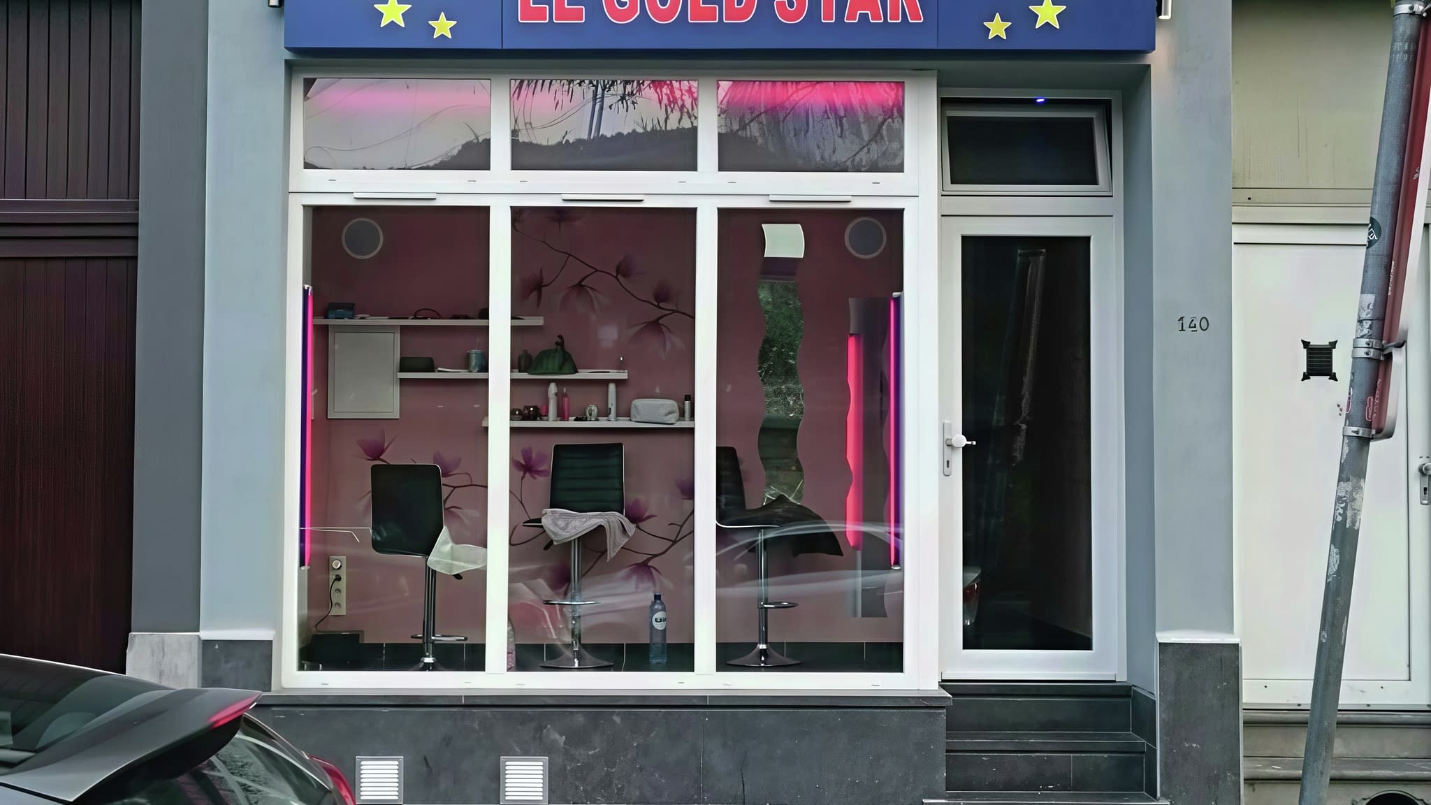 Екстериор на фризьорски салон „Le Gold Star“ със синя светеща табела и витрини, осветени в розово – пример за ефектна рекламна визия.