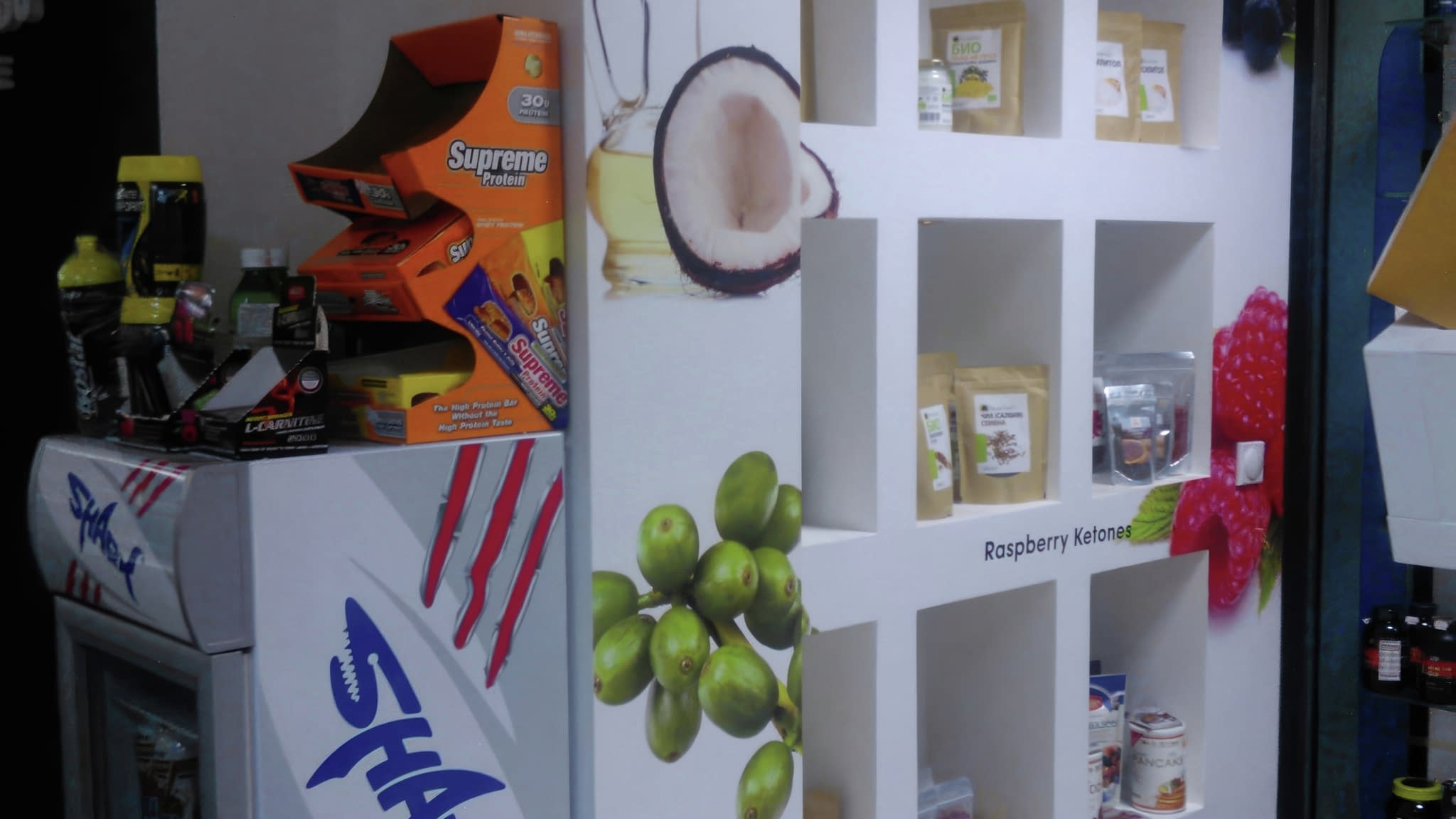 Изложба на здравословни продукти в магазин – брандирани ниши със суперхрани, обособени с рекламни лепенки, до хладилник с енергийни напитки Shark.