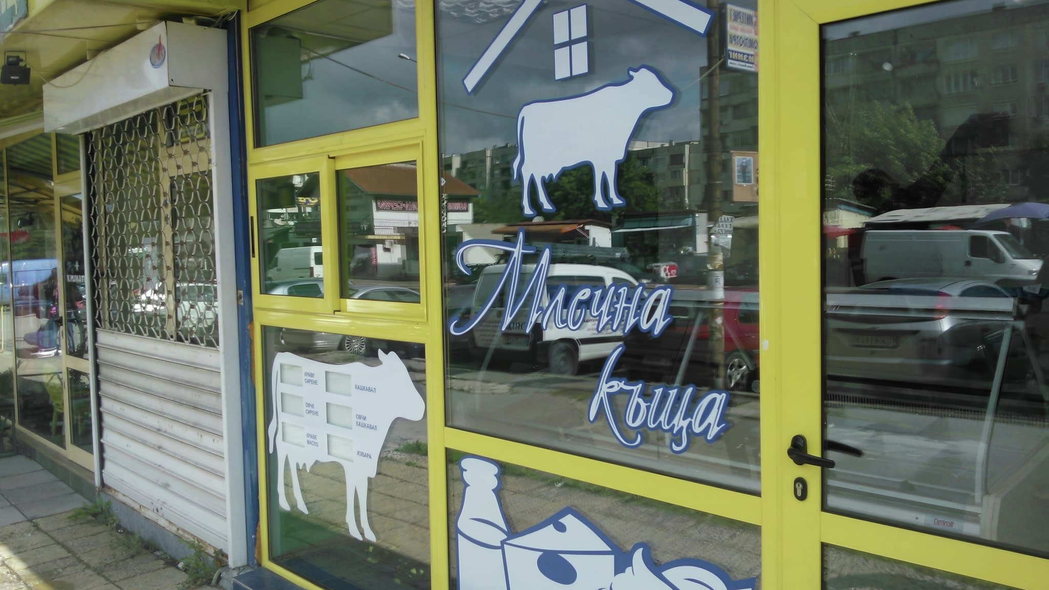 Витрина на млечен магазин с жълти рамки и сини надписи.