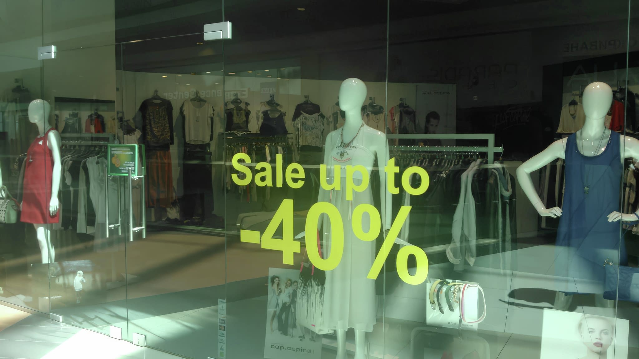 Витрина на магазин с рекламно фолио „Sale up to -40%“, представящо сезонни намаления с манекени в летни тоалети.