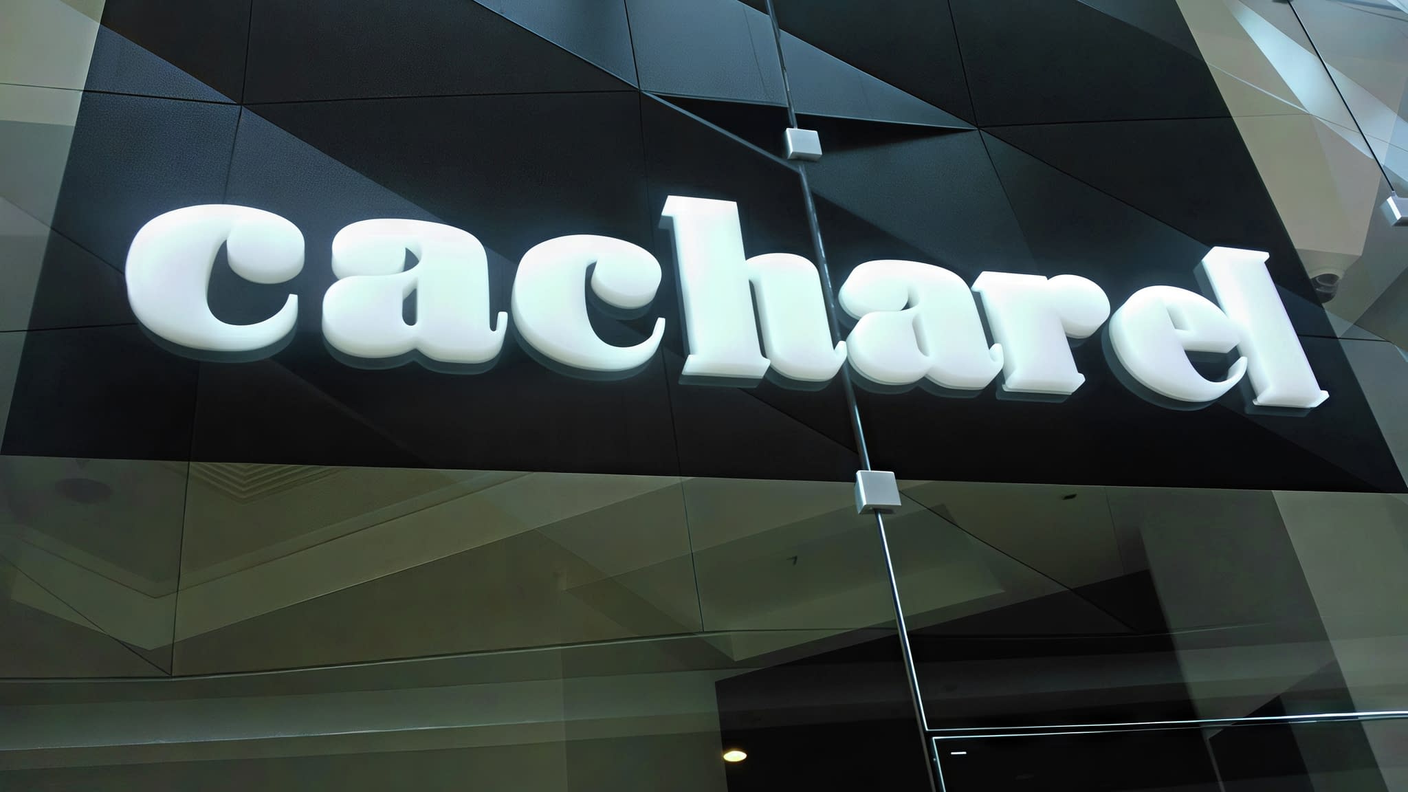 Релефна светеща табела с обемни букви 'Cacharel' в бял цвят, поставена на черна фасада – пример за брандова външна реклама.