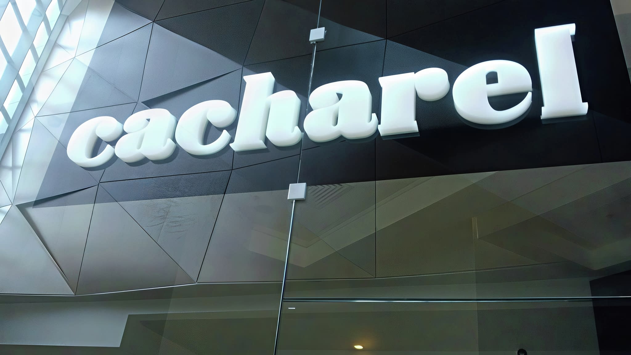 Обемни букви от плексиглас с надпис „cacharel“ в бял цвят, поставени върху черен фон на стъклена фасада.