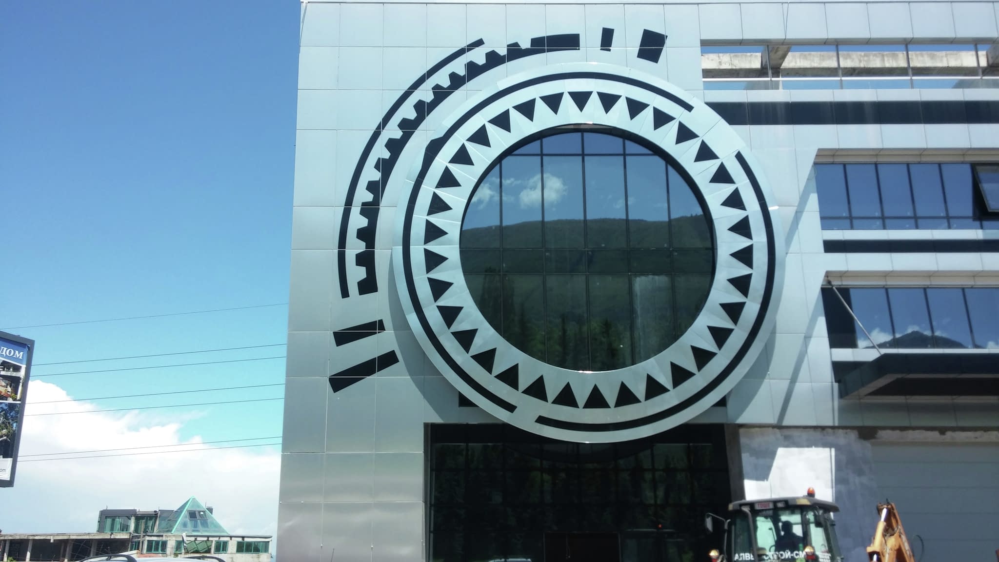 Информационна фасадна табела с голям кръгъл орнамент на стъклена сграда – професионален рекламен елемент за фирмен облик.