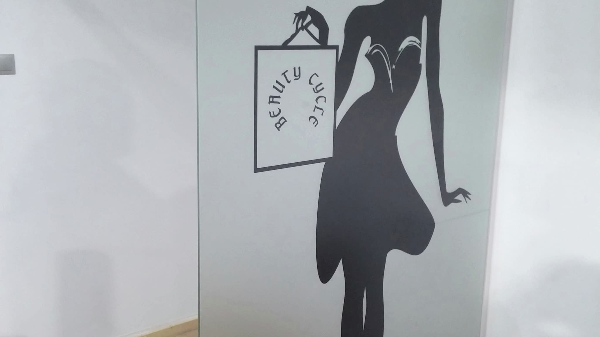 Панел от матирано стъкло с елегантен силует на жена в рокля, държаща пазарска чанта с надпис „Beauty Cycle“ – стилна интериорна декорация за салон или търговско пространство.