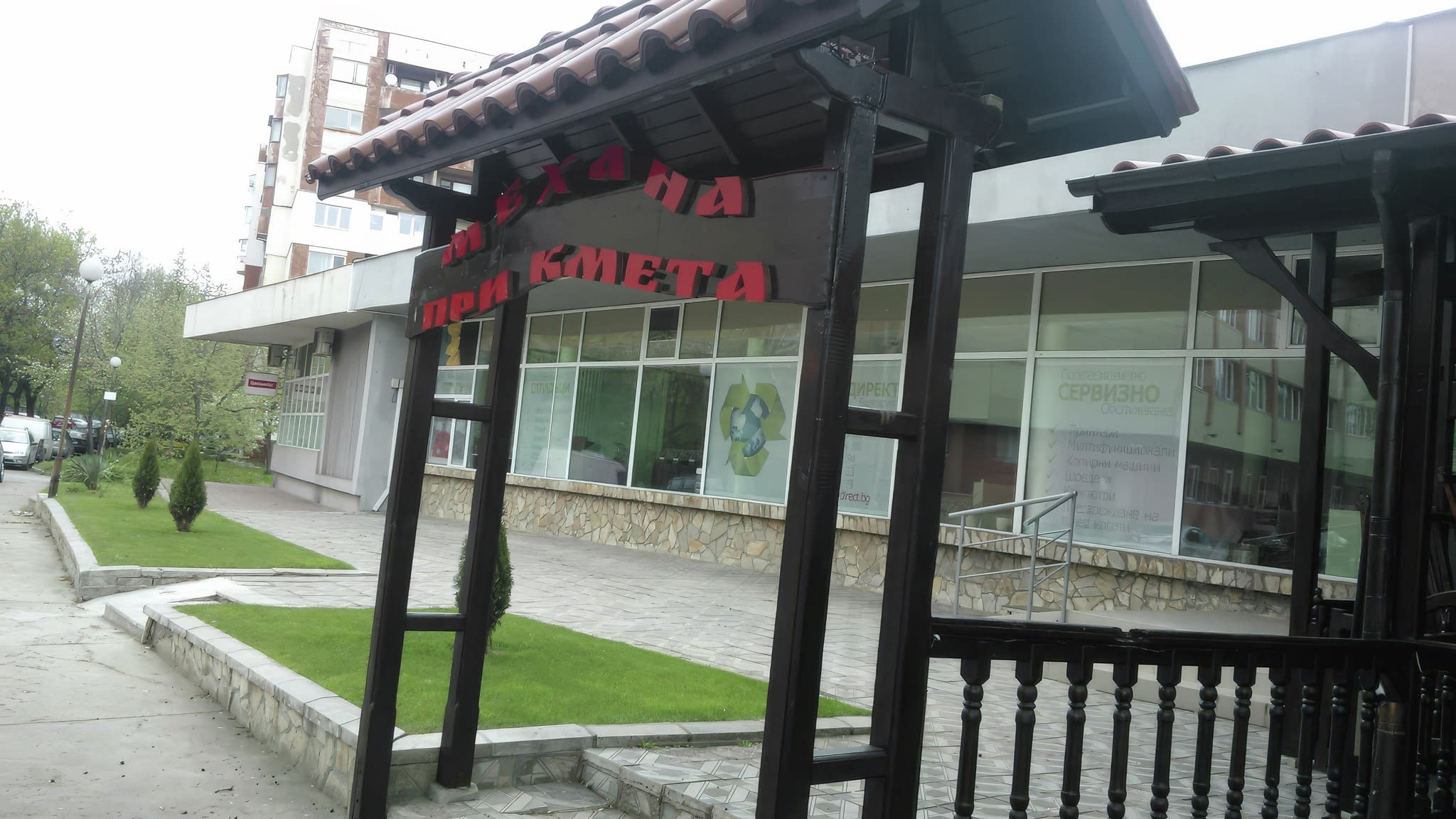 Дървена арка с керемиден покрив и червен надпис „Механа при кмета“, разположена пред входа на традиционно заведение.