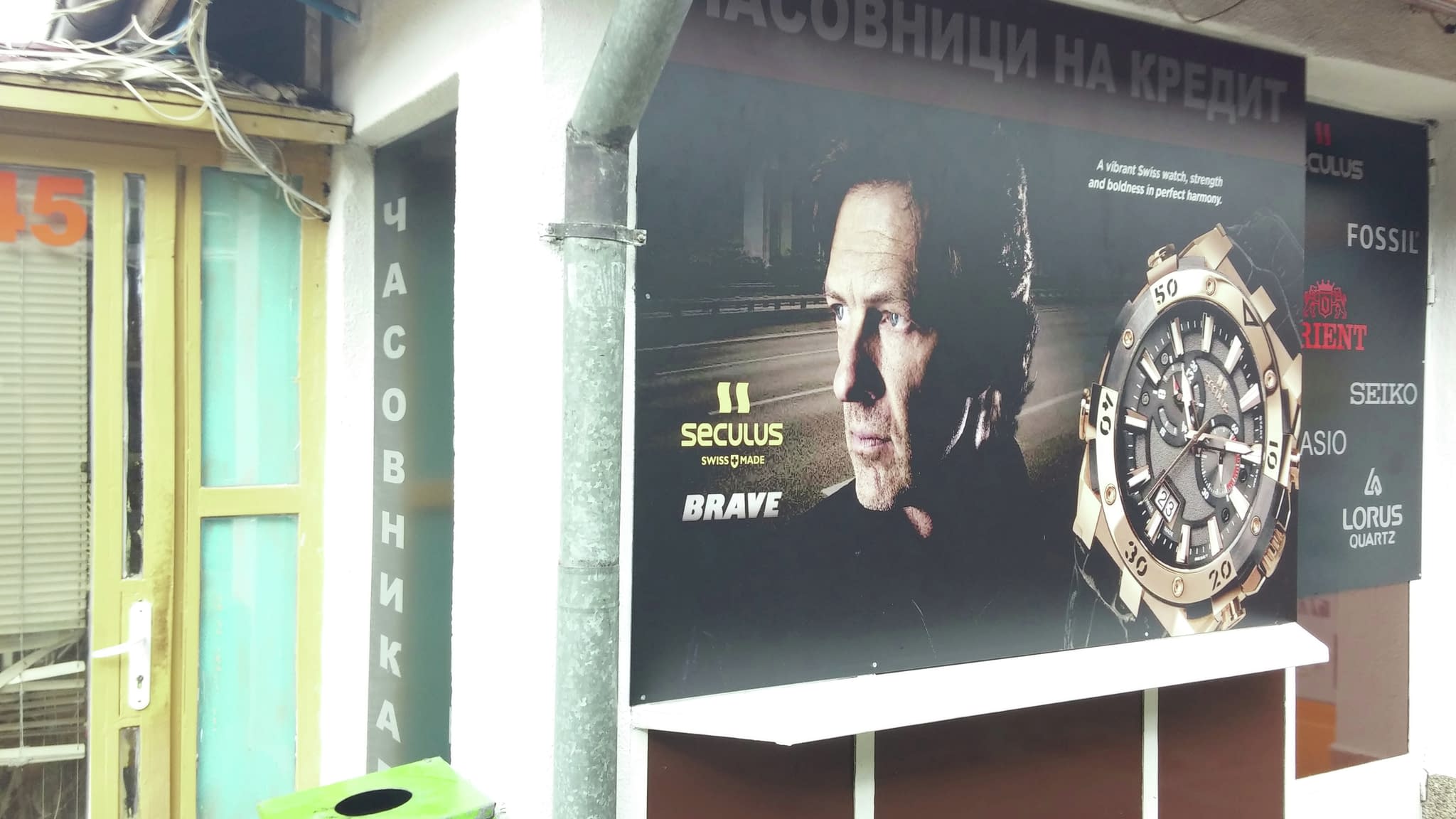 Витрина на часовникарски магазин с рекламна табела за продажба на часовници на кредит, голям дисплей с часовник Seculus и лога на популярни марки часовници.