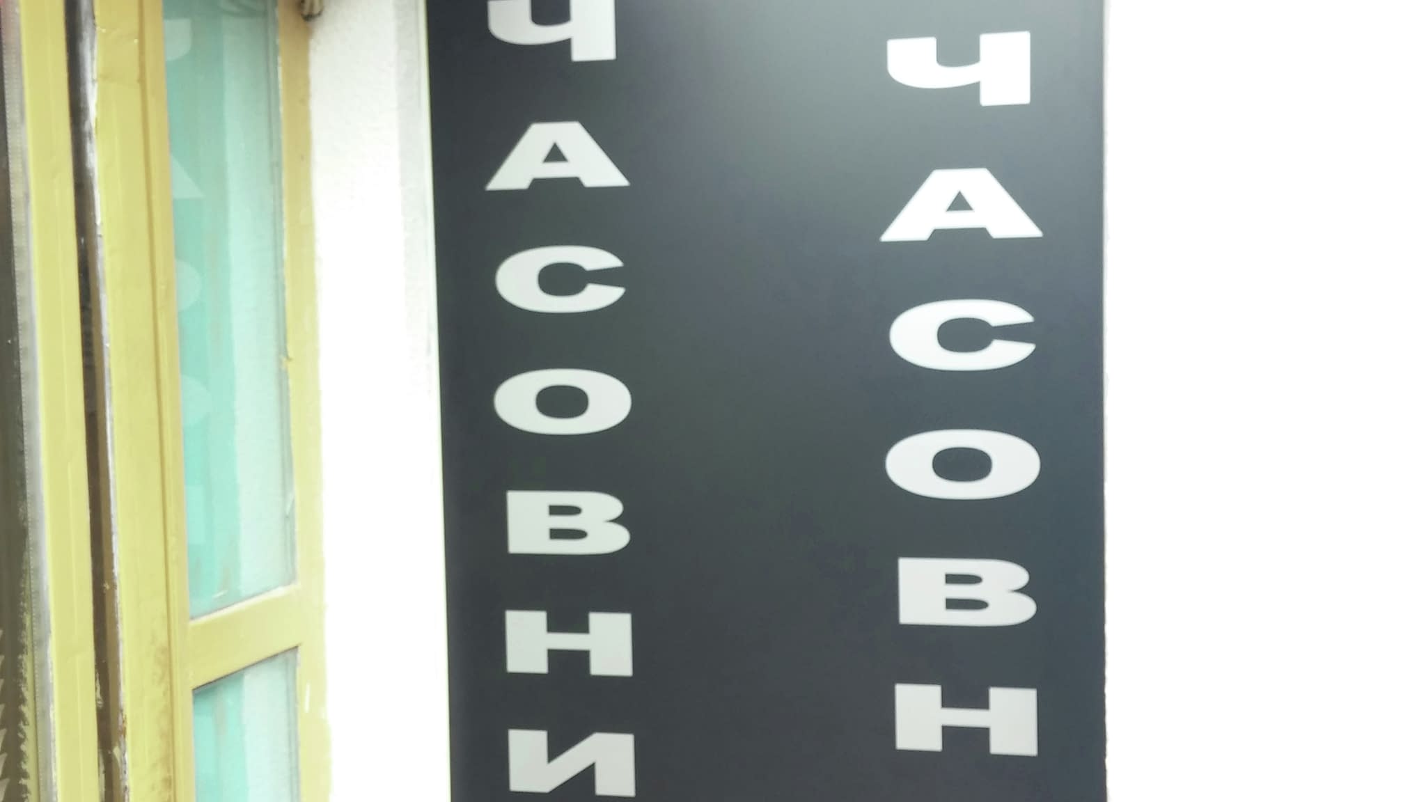 Черна рекламна табела със сребърни букви „Часовникар Часовници“, обозначаваща магазин за ремонт и продажба на часовници.