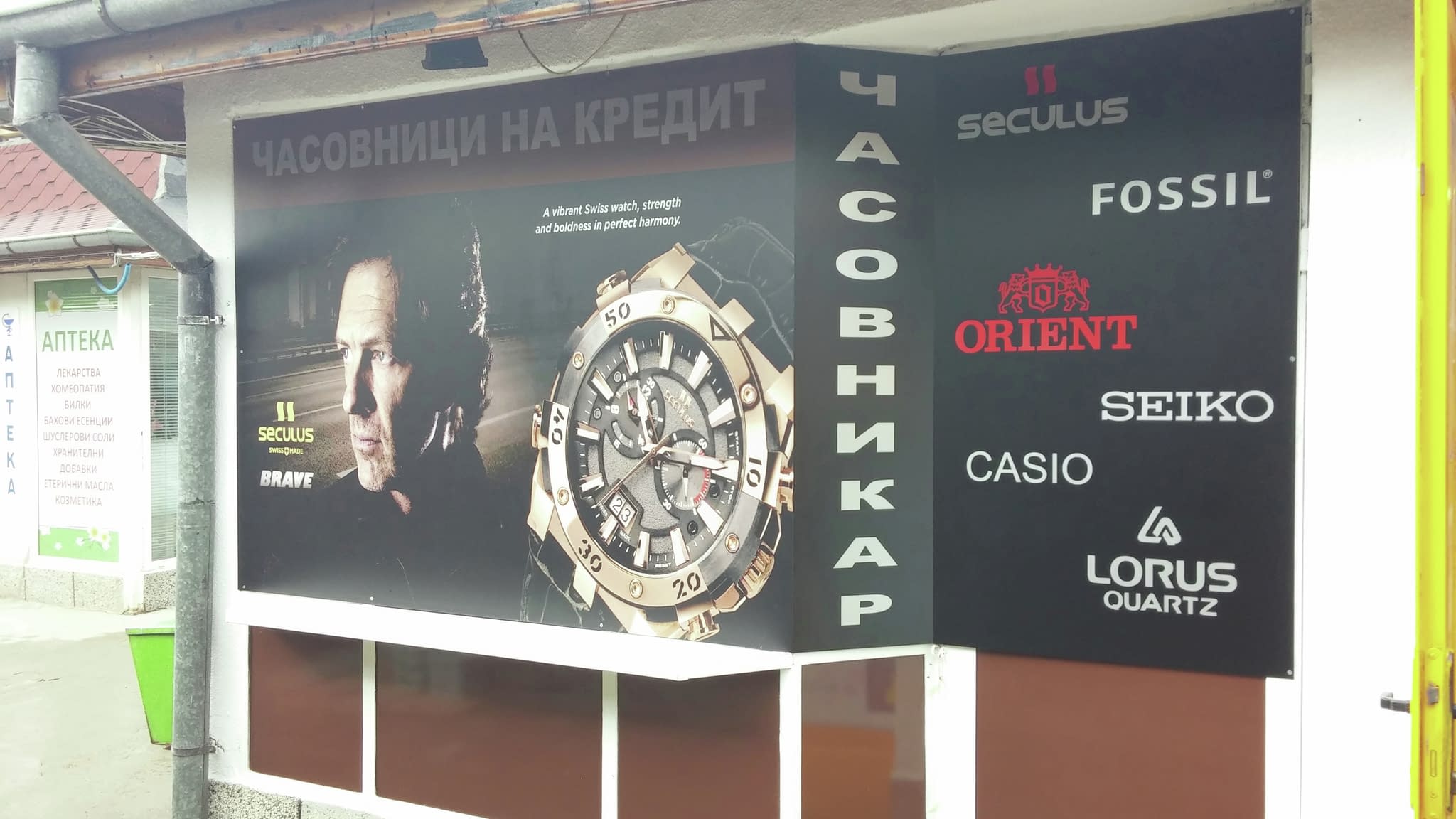 Рекламна витрина с портрет на мъж, голям часовник и лога на марки часовници - Seculus, Fossil, Orient, Seiko, Casio и Lorus.