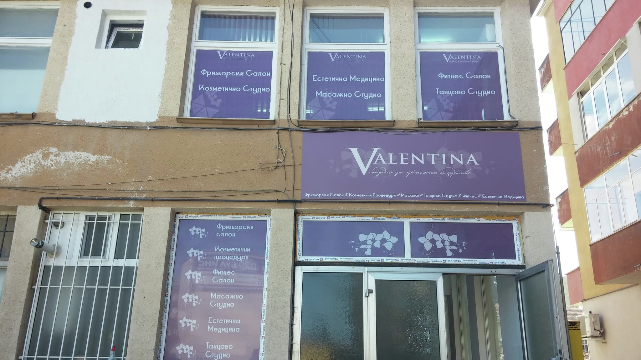 Външен изглед на салон за красота и wellness ‘Valentina’ с рекламни надписи на прозорците, посочващи предлаганите услуги – фризьорски салон, козметични процедури, масажно и танцово студио.