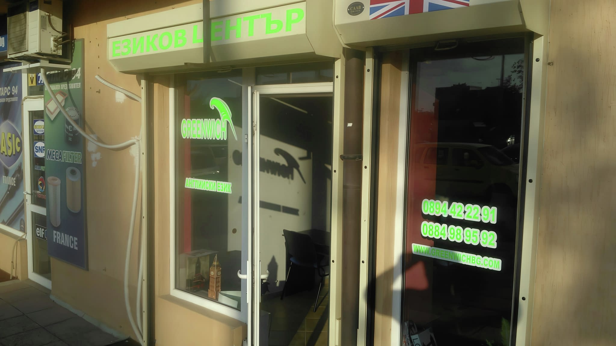 Витрина на езиков център „Greenwich“ със зелени надписи, информация за контакт и британско знаме над входа.