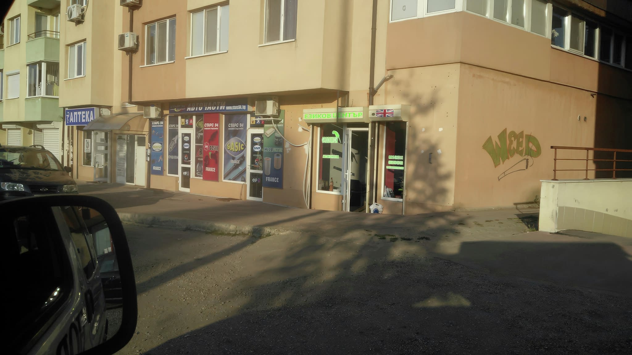 Отдалечен изглед на езиков център „Greenwich“ с брандирана витрина, зелени надписи и рекламно фолио.