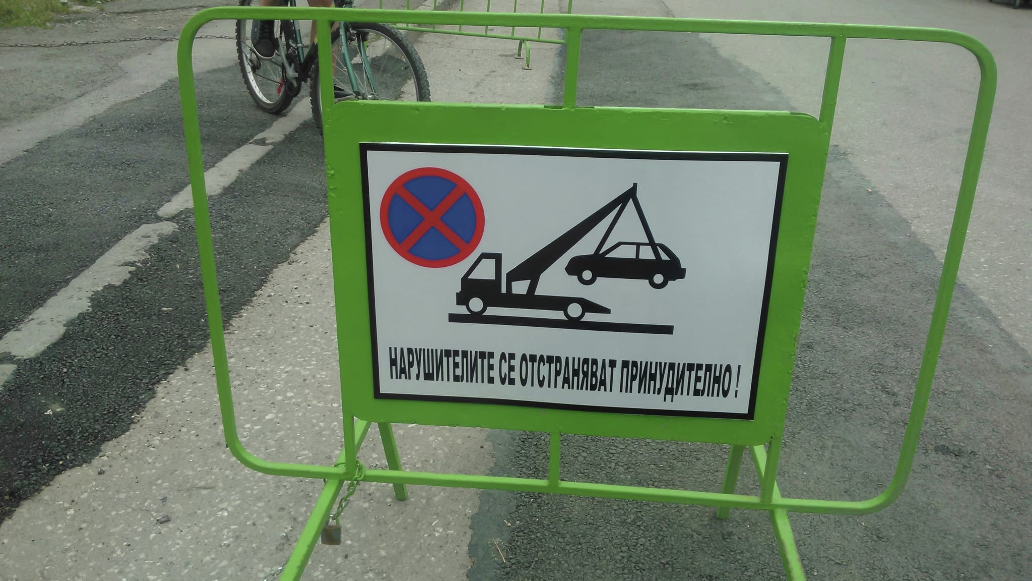 Пътен знак за забранено паркиране с предупреждение за репатриране, поставен върху зелена мобилна бариера на паркинг.