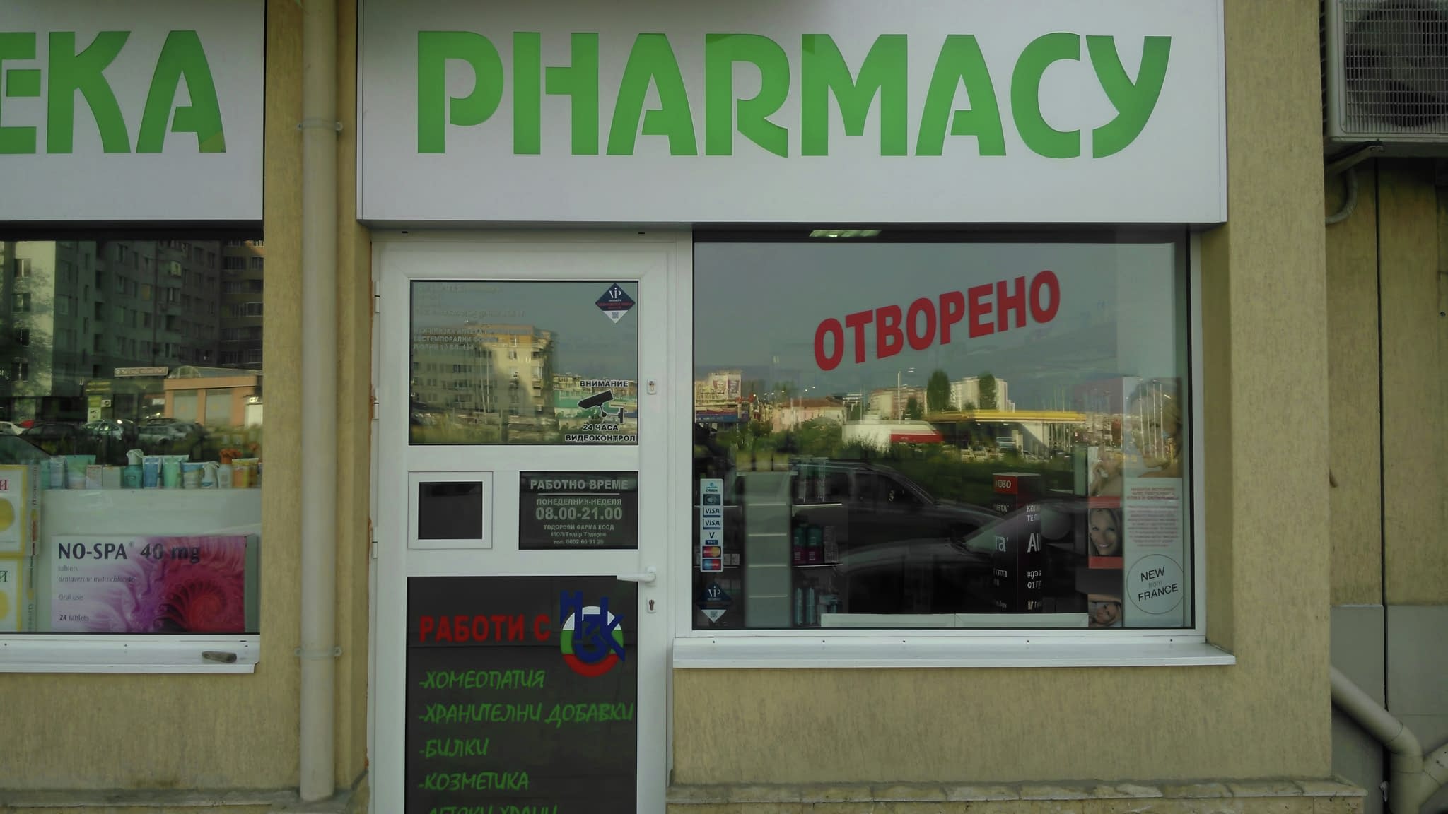 Вход на аптека с LED табела 'АПТЕКА' на български и 'PHARMACY' на английски, заедно с червен светещ знак 'ОТВОРЕНО' на витрината.