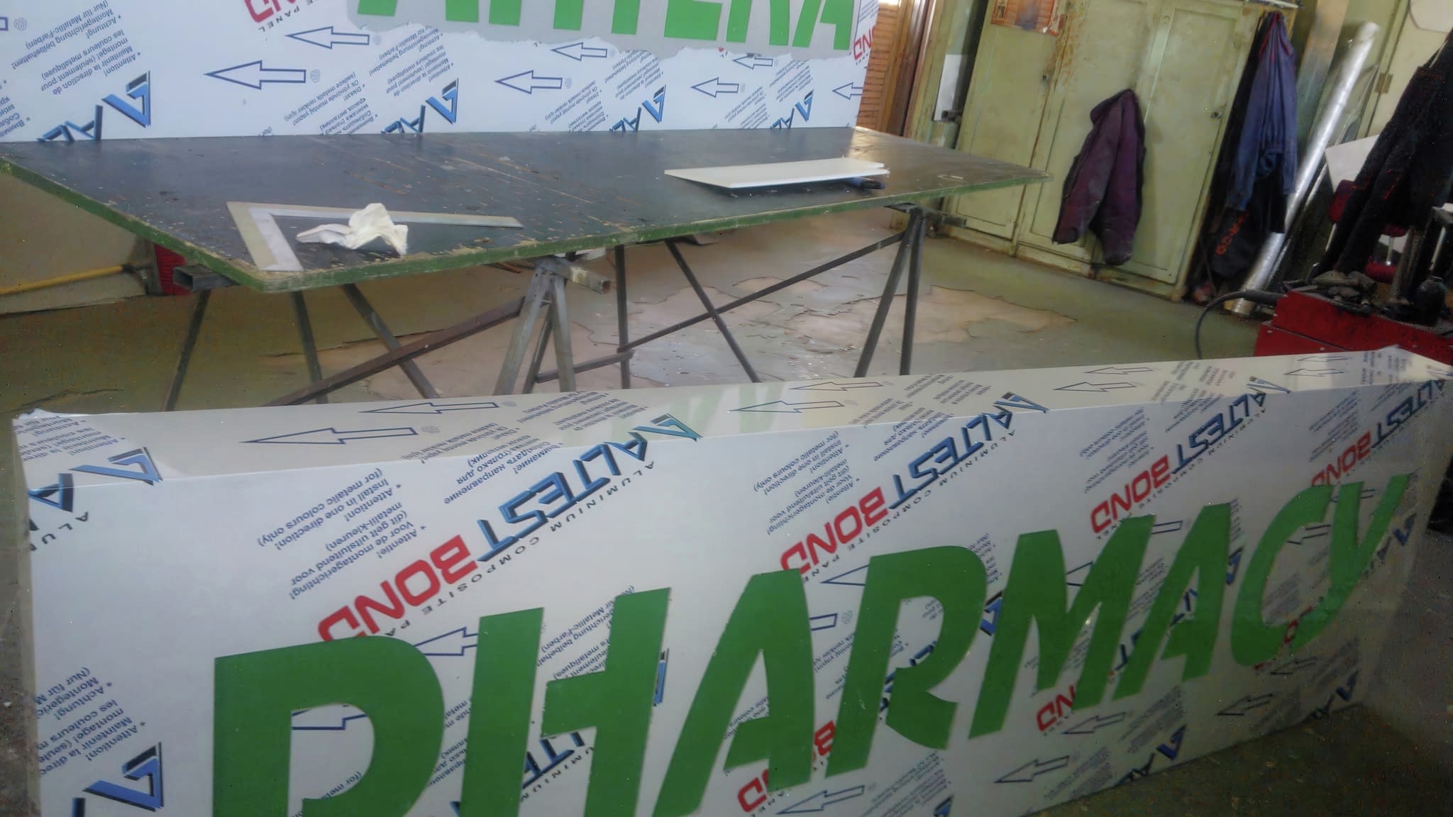 Работилница за изработка на светещи табели с големи зелени надписи 'АПТЕКА' и 'PHARMACY' – процес на създаване на рекламни табели.