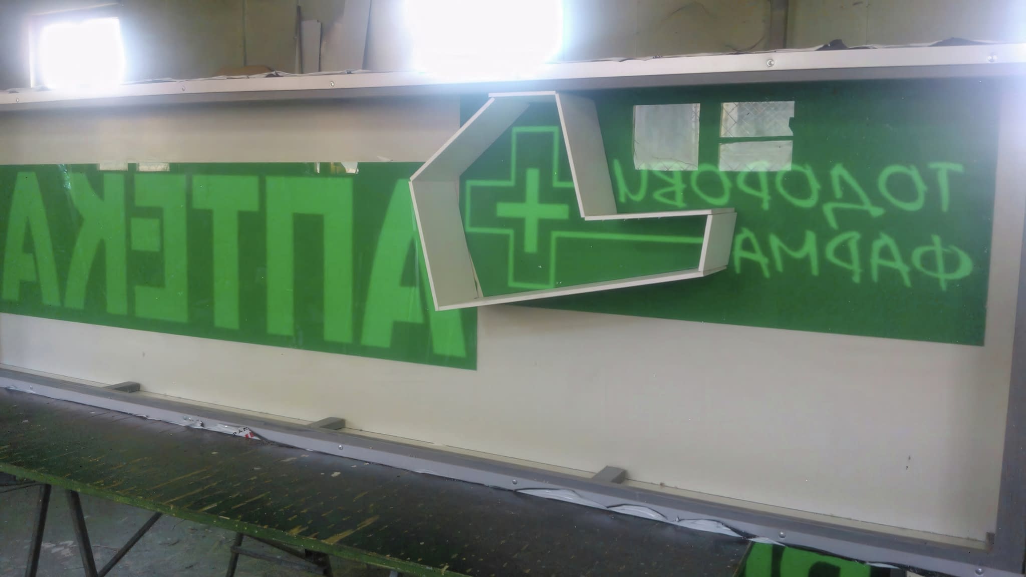 Частично завършена светеща табела за аптека със зелени букви 'АПТЕКА' и символ на медицински кръст – пример за LED реклама в процес на изработка.