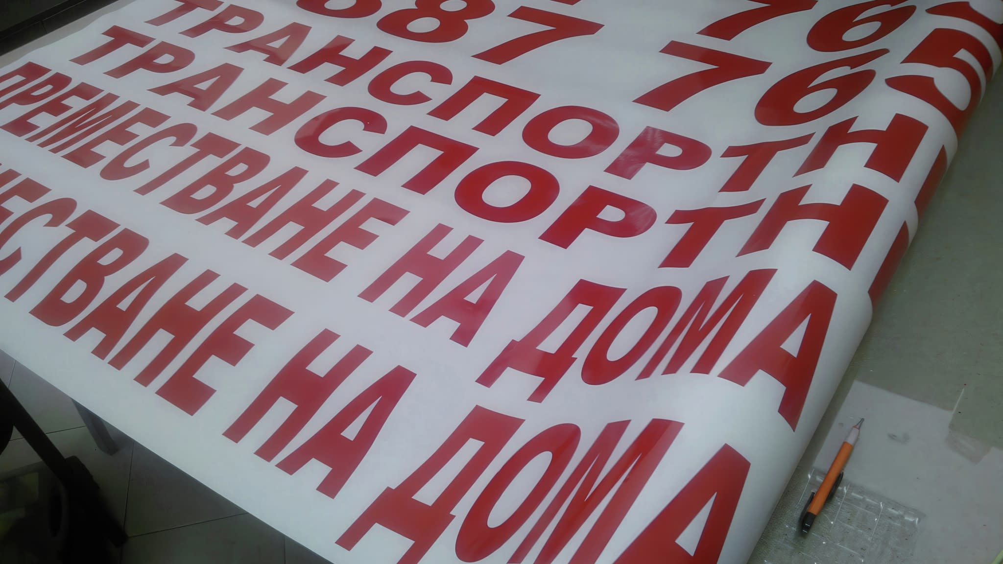 Лист с червени надписи, изрязани с плотер, включващи рекламни текстове за транспортни услуги и преместване на дома.