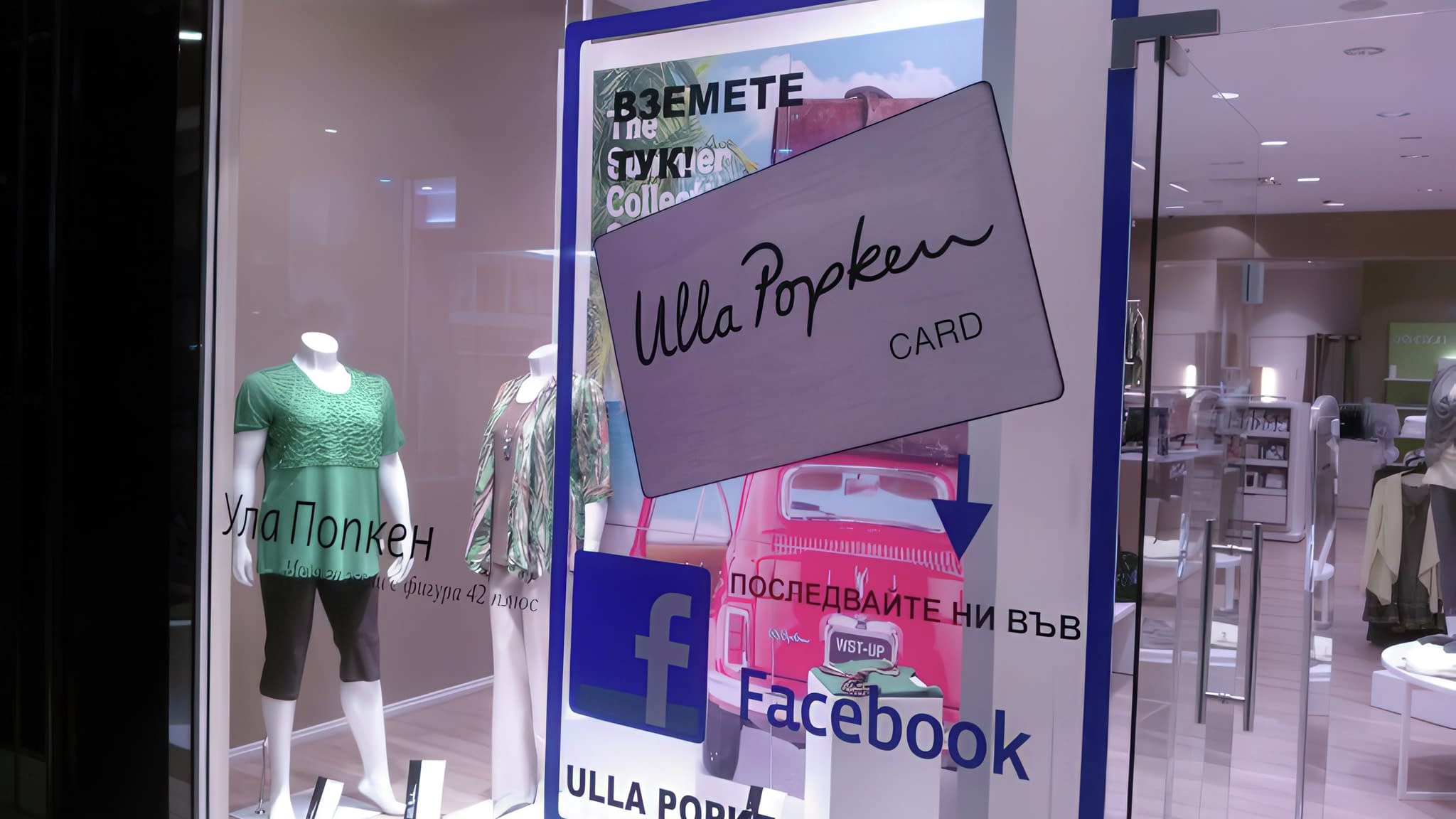 Витрина на магазин Ulla Popken с манекени в дамско облекло, рекламен надпис с карта за отстъпки и покана за следване във Facebook.