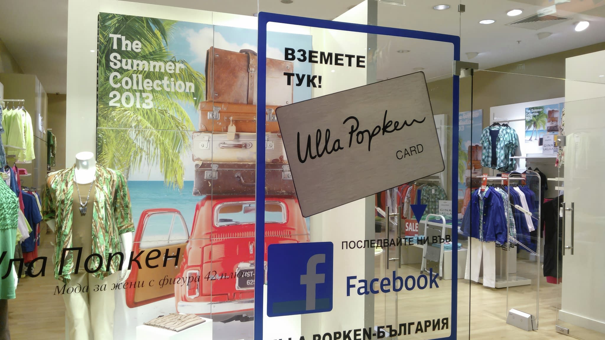 Вход на магазин Ulla Popken с надпис от самозалепващо фолио, показващ промоционална карта и покана за следване във Facebook.