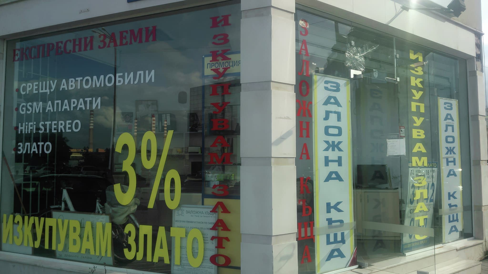Рекламно фолио на заложна къща – голяма витрина с цветни изрязани букви „Изкупувам злато“ и „Бързи заеми“ в червено и жълто, и промоционален процент за заеми.