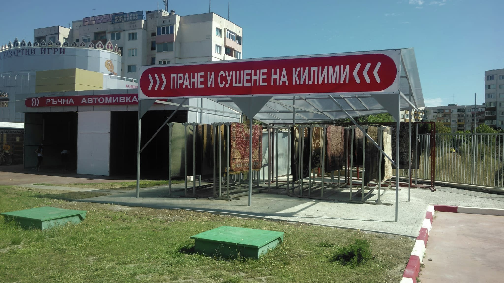 Рекламни винилови пана с надписи 'Ръчна автомивка' и 'Пране и сушене на килими', монтирани на навеси в автомивка.