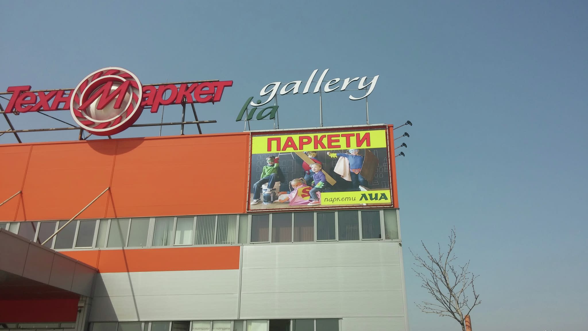 Голямо винилно рекламно пано с деца и надпис 'Паркети Лиа', монтирано на фасадата на търговски център.