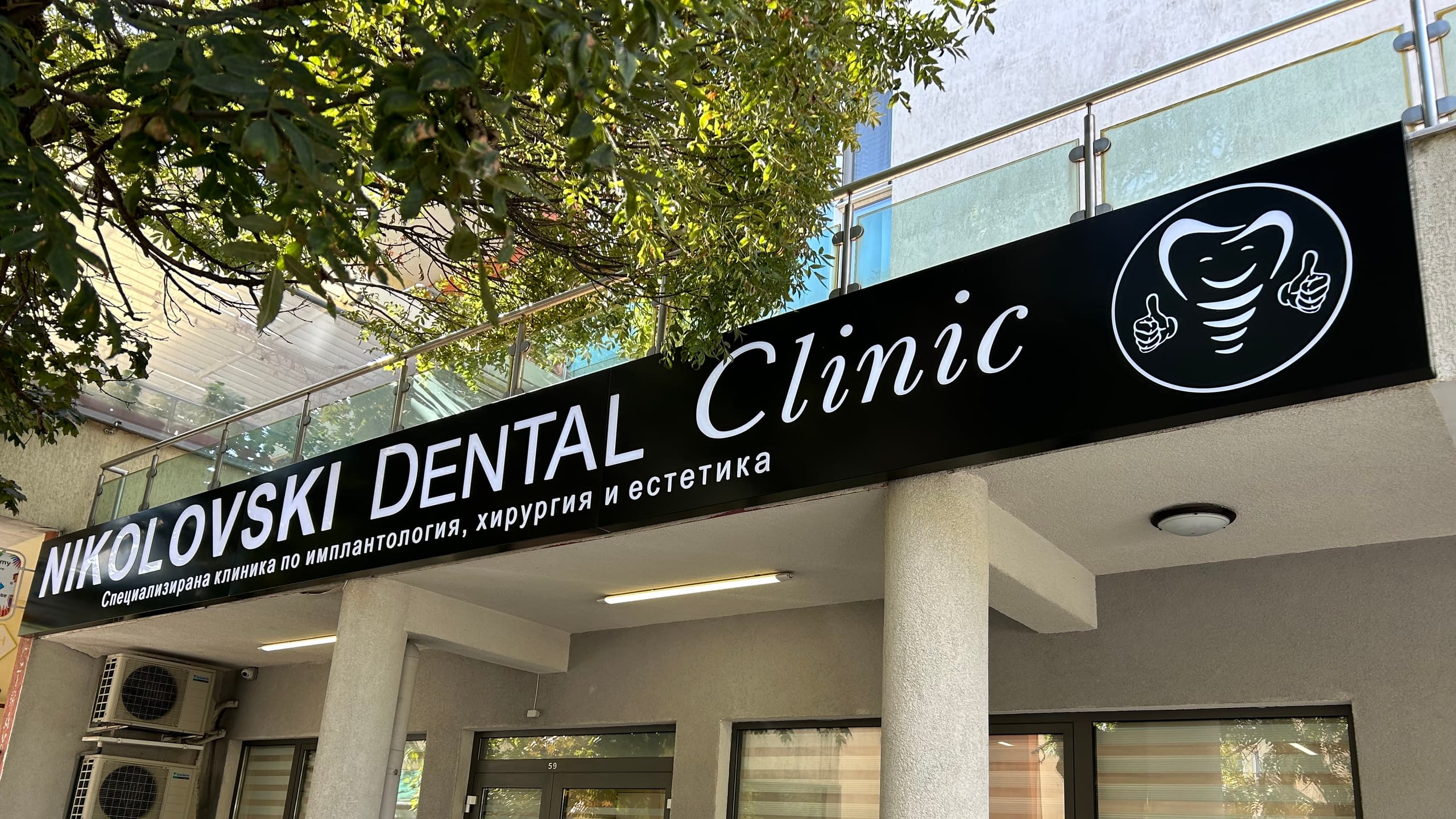 Светещо рекламно табло за "Nikolovski Dental Clinic", монтирано на фасадата на сградата. Табелата е черна с бял надпис и лого на зъб.