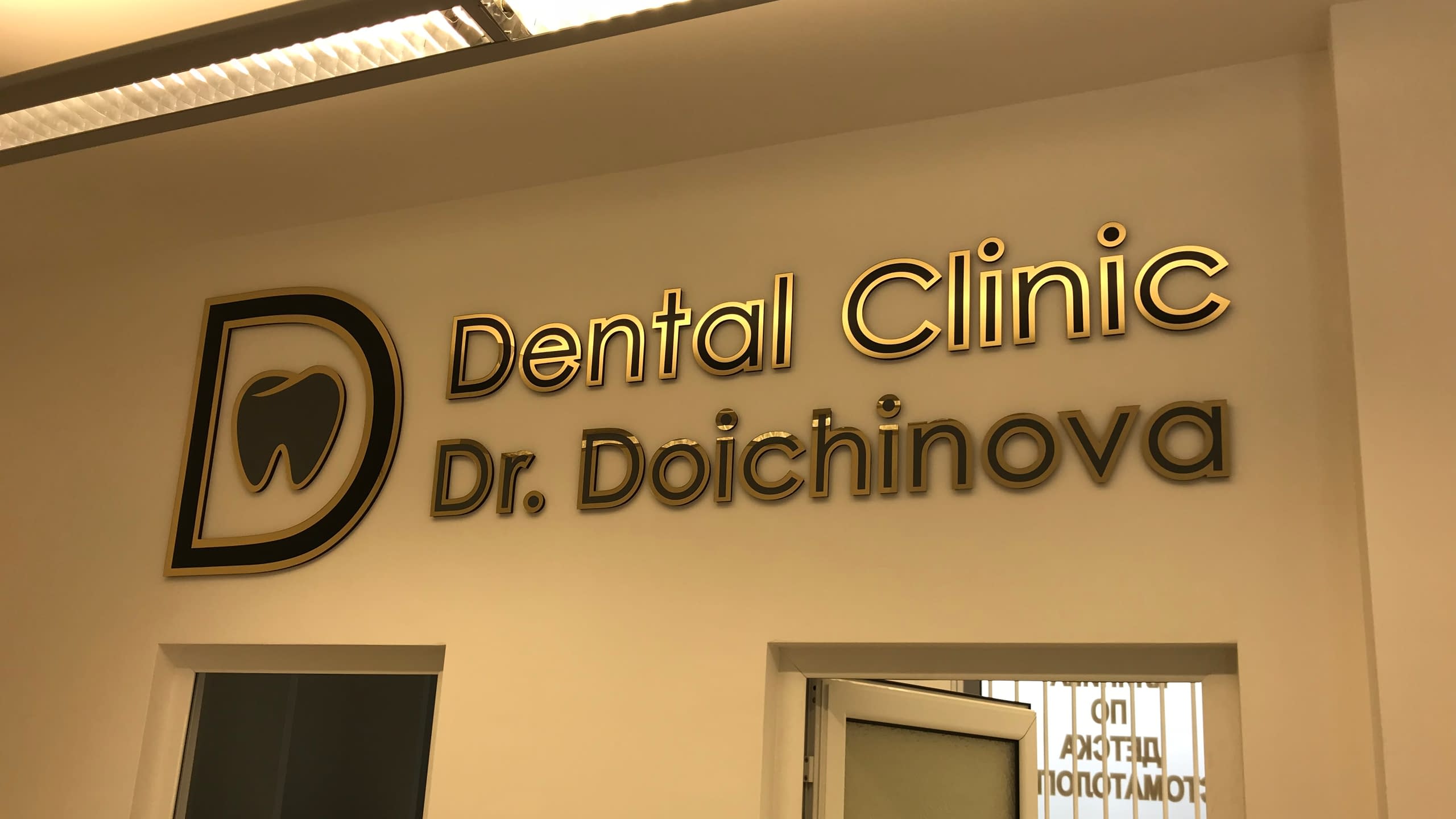 Интериорна офис табела с обемни букви в златисто и черно за "Dental Clinic Dr. Doichinova", монтирана на стена над врата.