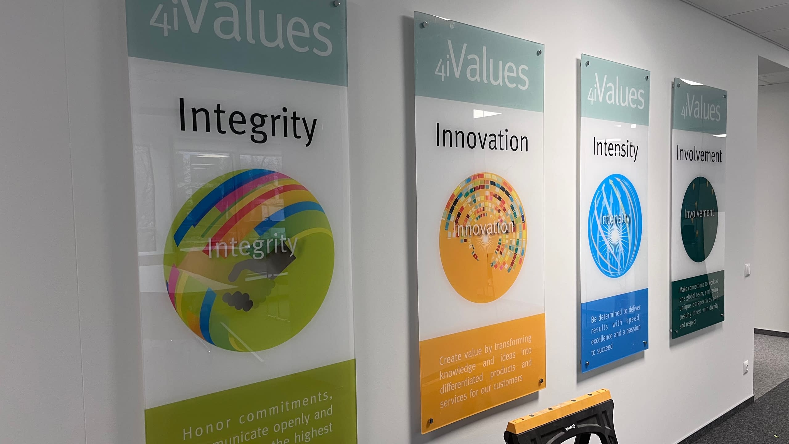 Серия от четири вертикални информационни табели от плексиглас за фирма "4Values", монтирани с дистанционери на стена в офис.